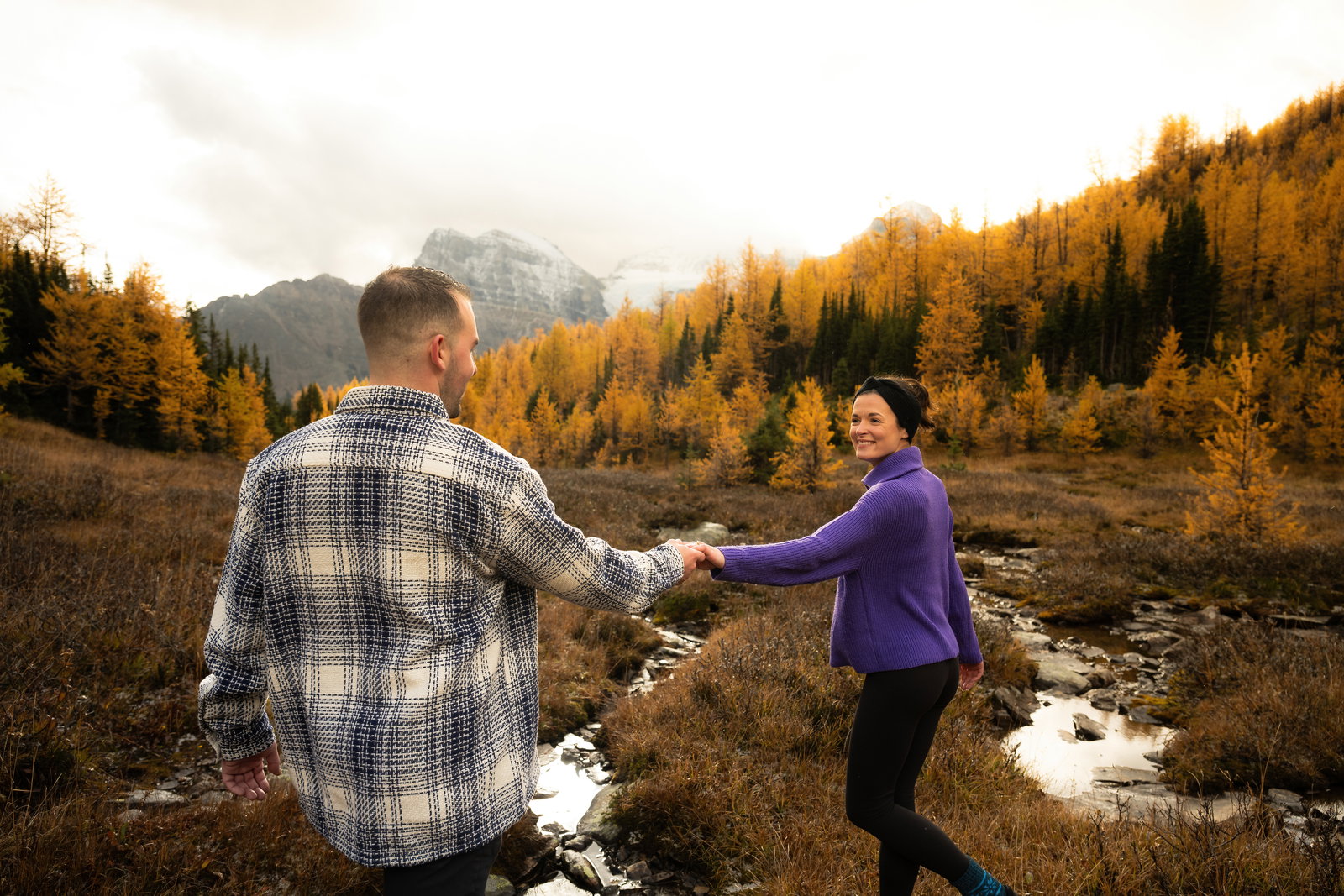 A couple dancing in a field of golden larches with mountains in the background.