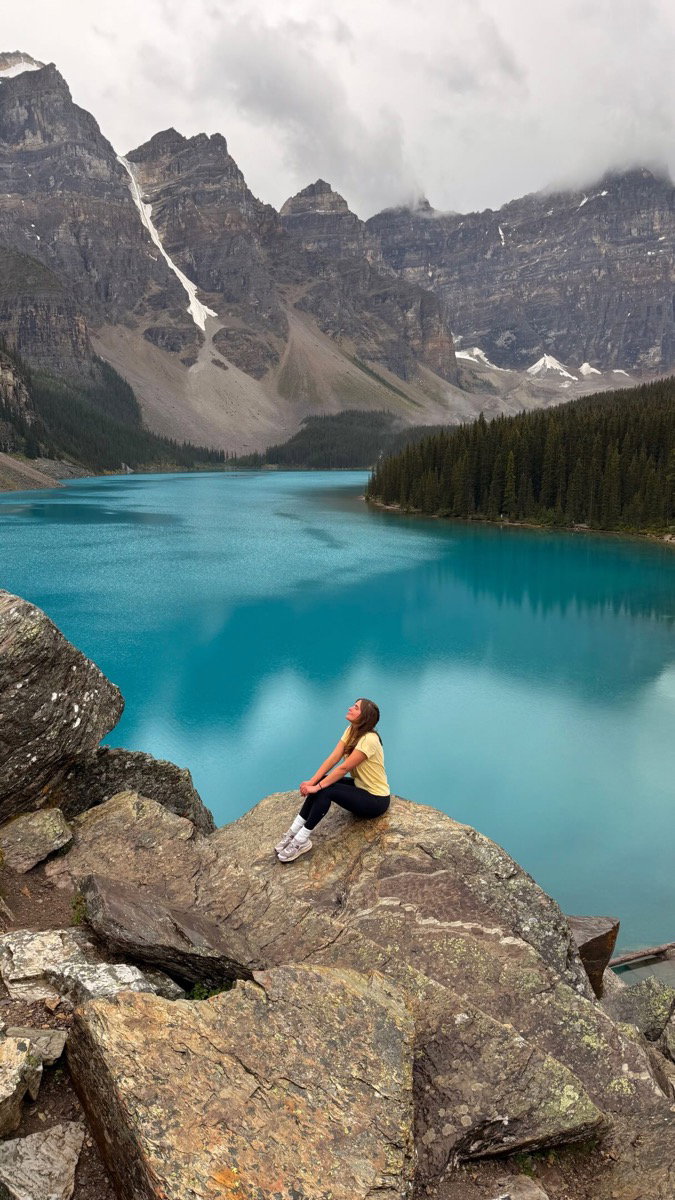 Hiker sitting on rocks above turquoise Moraine Lake beneath the Valley of the Ten Peaks