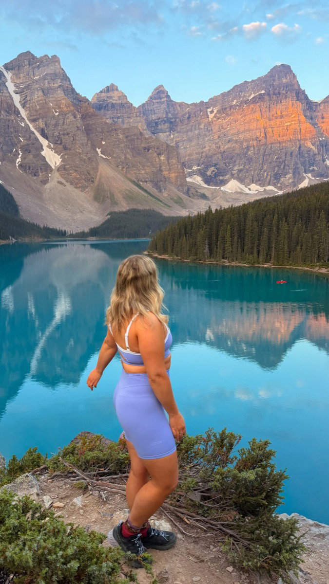 Woman in hiking clothes standing above turquoise Moraine Lake and the Valley of the Ten Peaks