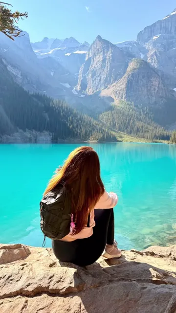Woman sitting on the rocky lakeshore beside turquoise Moraine Lake