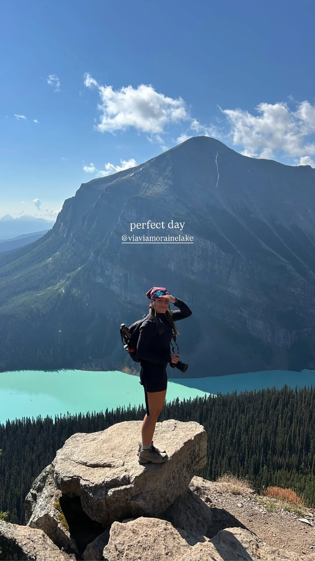 Hiker standing on a rocky overlook above a blue alpine lake and mountain valley