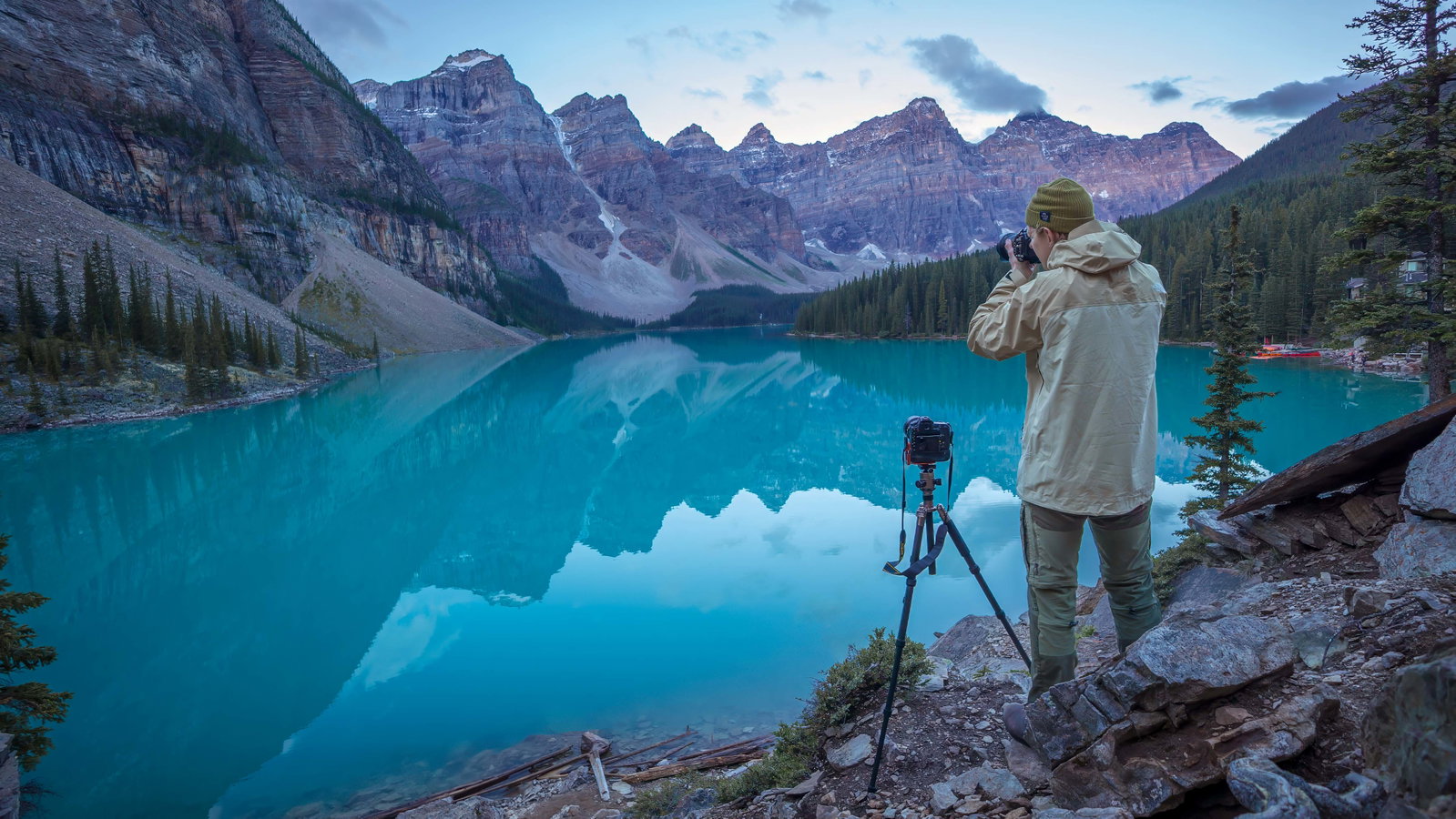 Photographer Will Lambert capturing sunrise at Moraine Lake with a camera and tripod on a rocky shore.